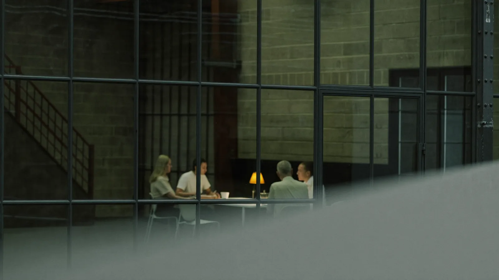 A meeting room seen through glass partitions, four people at a table, heavily defocused.